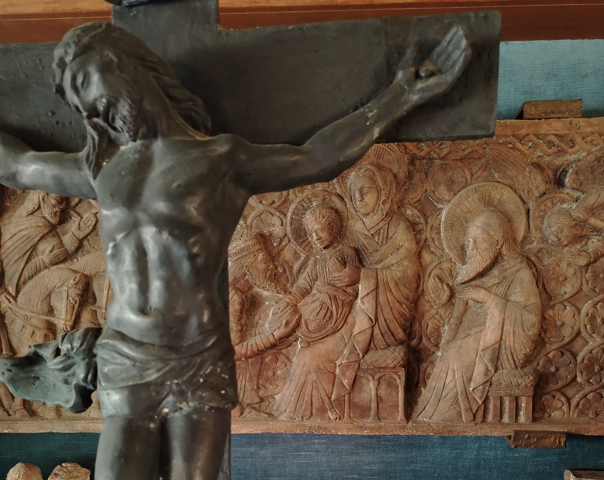 In primo piano crorifisso in bronzo, dietro  rilievo scultoreo in terracotta (romanico)
